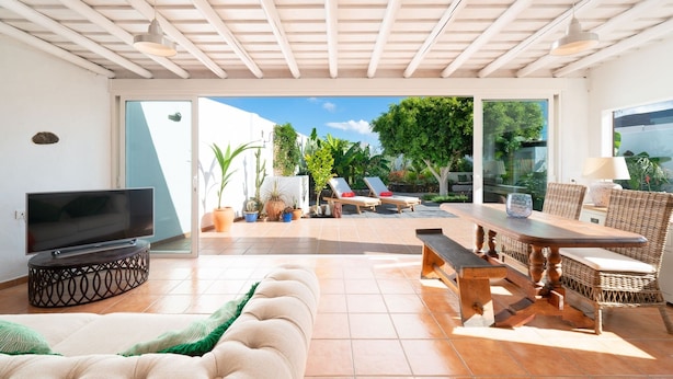 A spacious living area with a TV, sofa, and dining table. - Finca Botanico Secret Garden - Private Tropical Garden, BBQ, Outdoor Spa Shower (Guatiza)