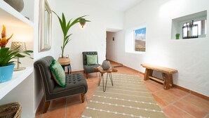 A spacious living area with a sofa, armchair, and a small wooden bench. There is a potted plant and a lamp on a side table. - Finca Botanico Secret Garden - Private Tropical Garden, BBQ, Outdoor Spa Shower (Guatiza)