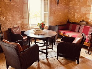 A cozy room with a round wooden table, wicker chairs, a cushioned sofa, and a patterned rug. - Tastefully renovated Cretan traditional house with large private pool (Gavalochori)