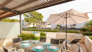 Un área de comedor al aire libre con una mesa de madera dispuesta para cuatro personas, sillas alrededor y una sombrilla que da sombra.