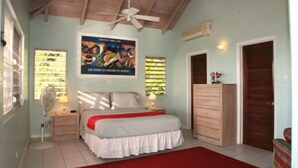Un dormitorio con cama, mesitas de noche, un ventilador, cómoda y ventilador de techo.