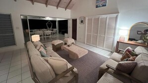 Sala de estar con un sofá, una mesa de centro y una mesa de comedor con sillas. Hay un ventanal corredero que da a un balcón.