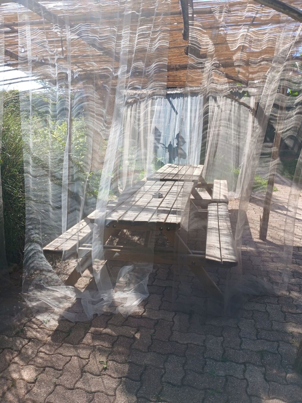 Un espacio de estar techado al aire libre con una mesa y bancos, rodeado por un dosel transparente.