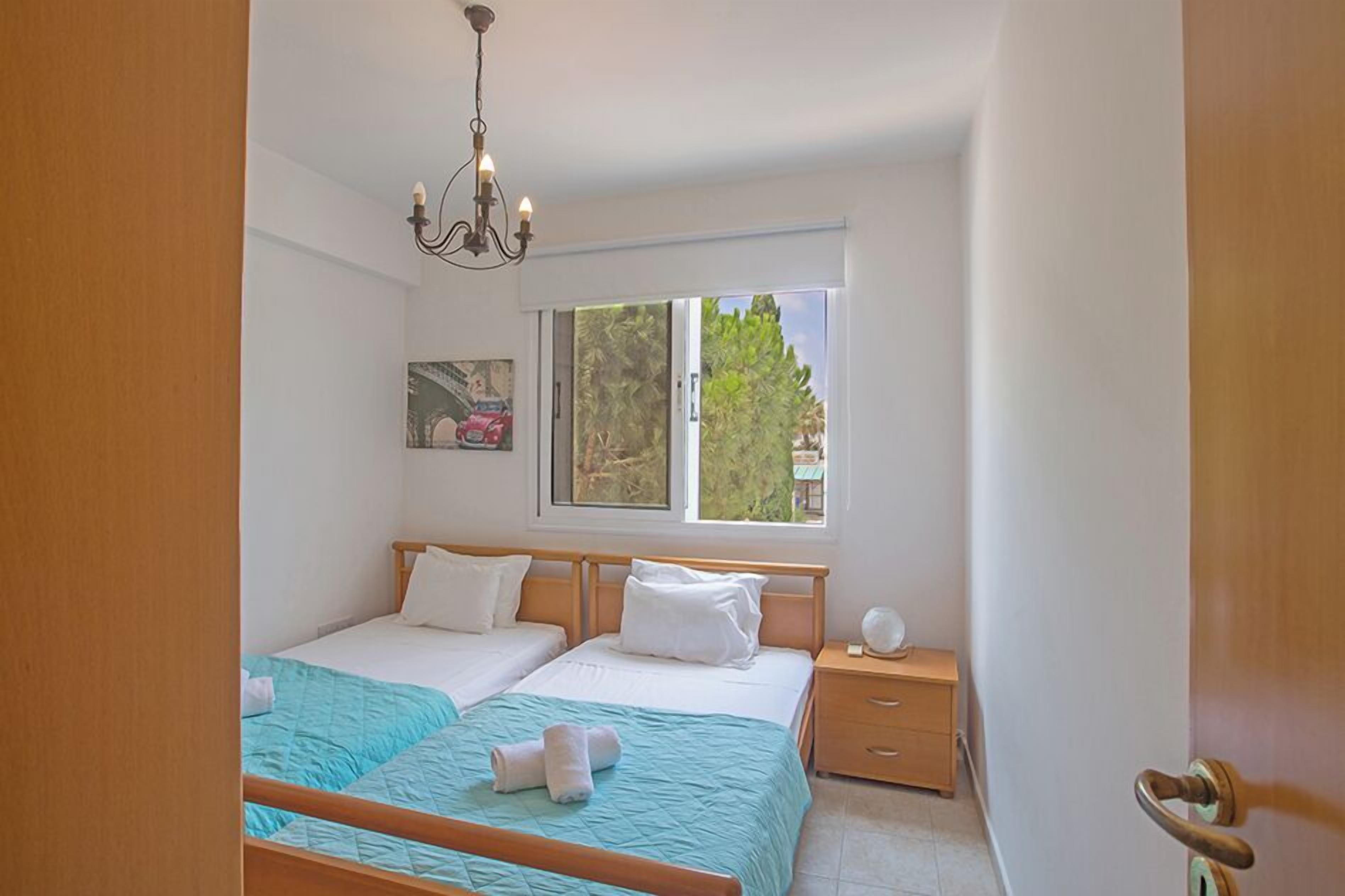 A bedroom with two beds, a nightstand, a chandelier, a window with a view, and a door.