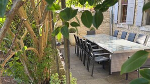 An outdoor patio with a long table and chairs, surrounded by greenery and a stone wall. - House with character (Montségur-Sur-Lauzon)