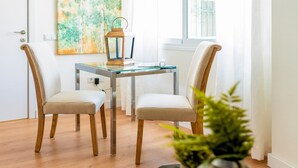 Un coin repas comprenant deux chaises, une table en verre, une lanterne en bois et un tableau accroché au mur.