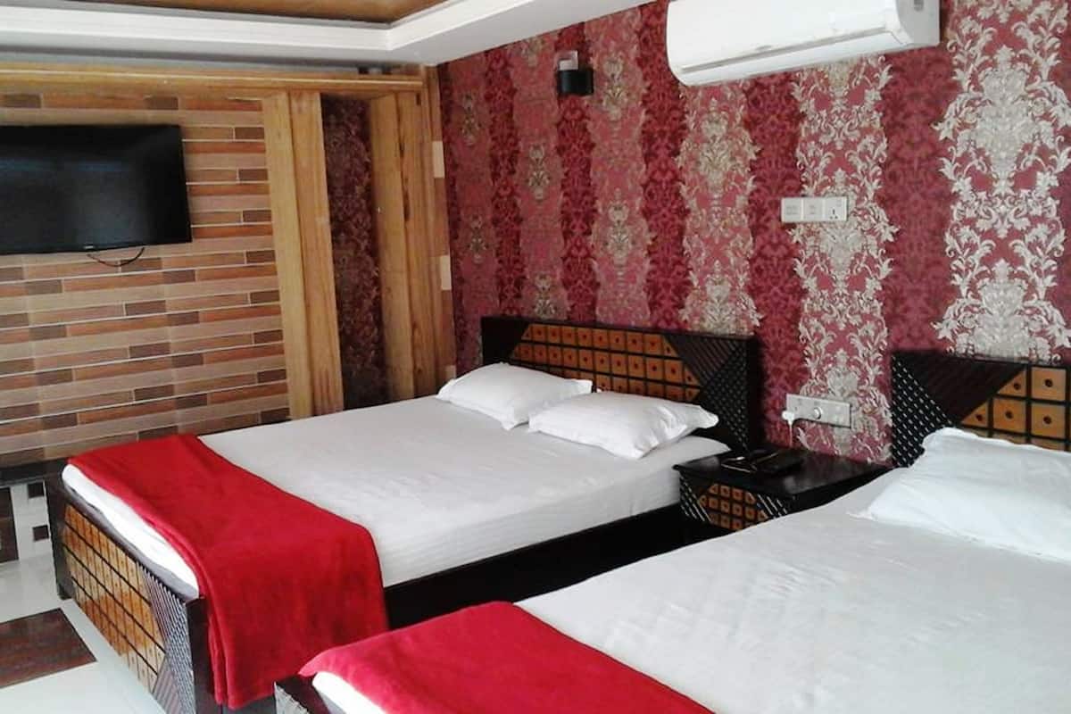 A hotel room with two beds, a TV mounted on the wall, and a patterned wallpaper.
