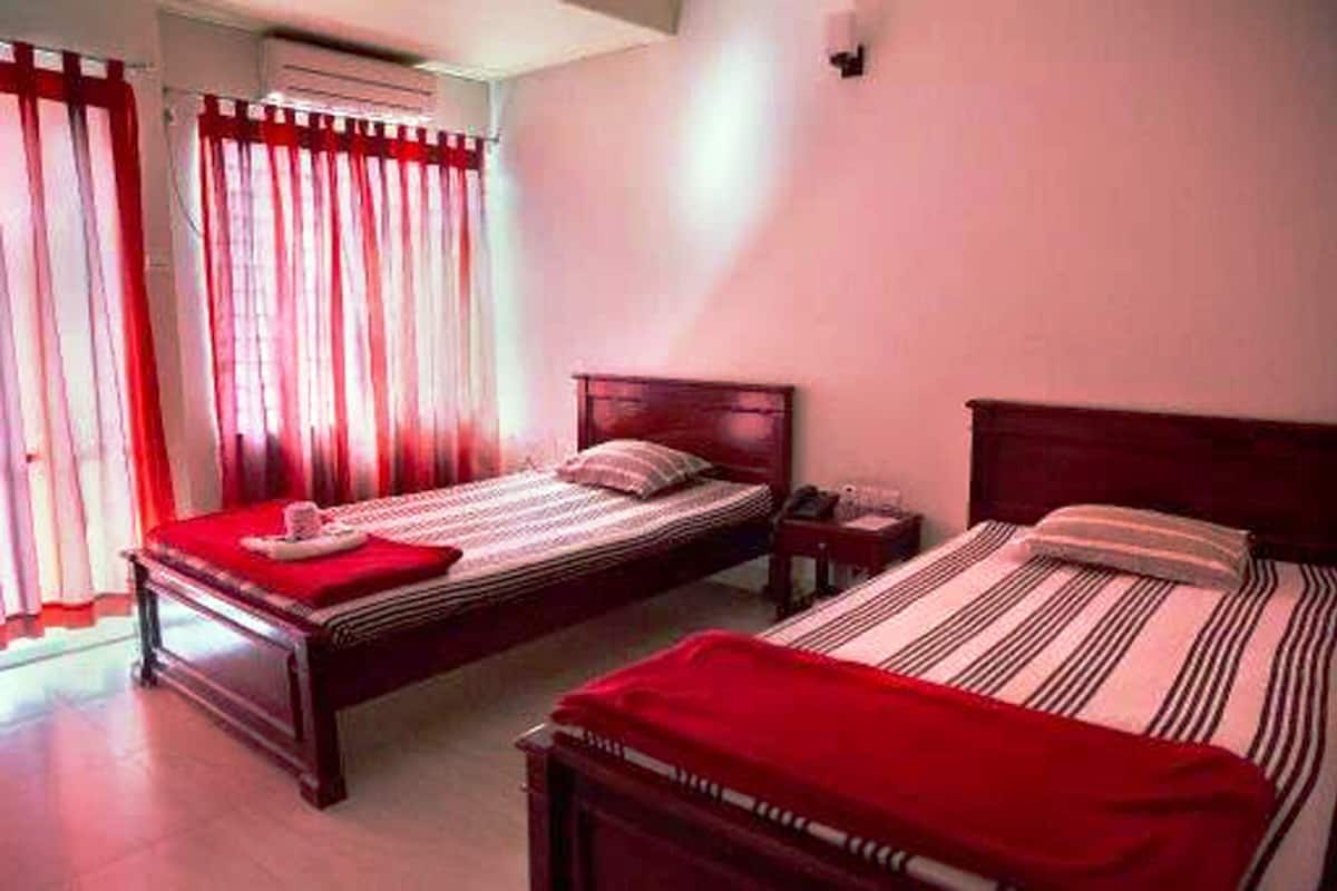 A hotel room with two single beds, each with a red blanket and a wooden headboard.