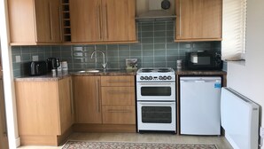 Una cocina compacta con armarios de madera, un lavamanos de acero inoxidable, una estufa blanca, un microondas y un refrigerador blanco.