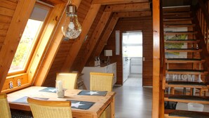 Un interno in legno con un tavolo da pranzo, sedie, una lampada a sospensione e una scala.