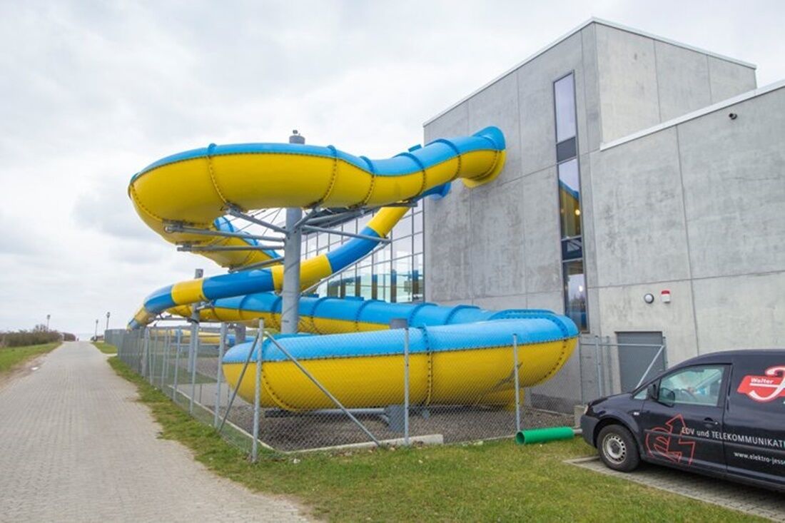 A water slide structure adjacent to a modern building with a metal fence.