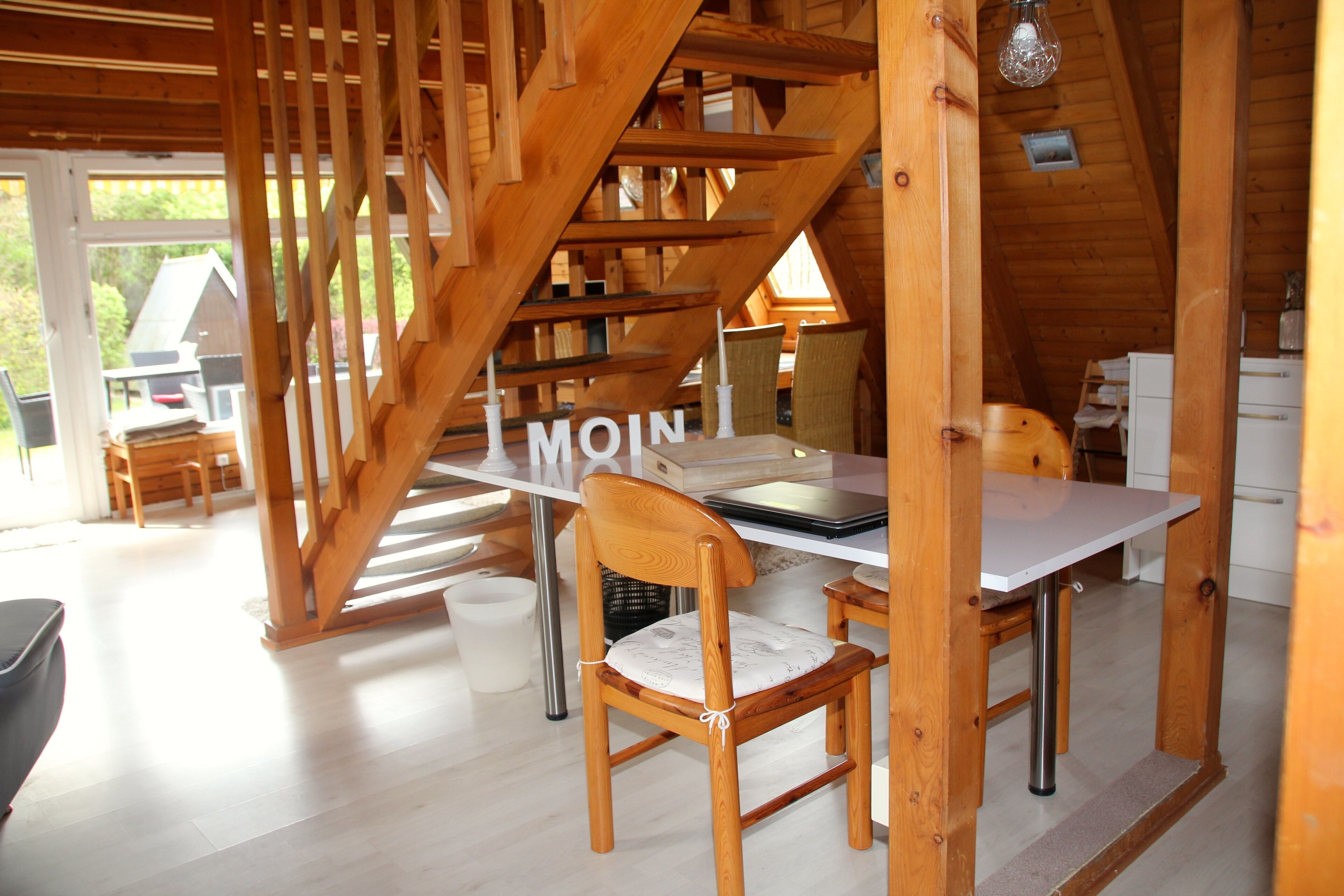 A wooden interior with a dining table and chairs, a staircase, and a view of the outside.
