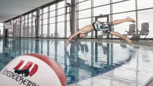 Un nuotatore esegue un tuffo in piscina, con un logo sul bordo.