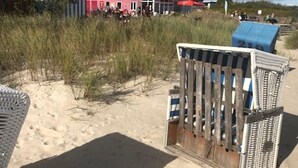 Un edificio fronte spiaggia con una facciata ben definita in rosso e bianco, un ingresso visibile e un primo piano sabbioso con sedie da spiaggia.