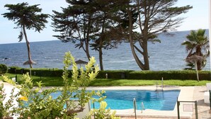 A pool area with a view of the sea, surrounded by trees and a well-maintained lawn. - Apartment Ocean Front - Rocas del Mar - Riviera del Sol. (Mijas Costa)