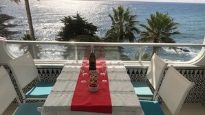 A table set with a bottle, glasses, and bowls of nuts and fruits on a balcony with a view of the ocean. - Apartment Ocean Front - Rocas del Mar - Riviera del Sol. (Mijas Costa)