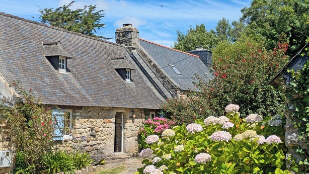 Ein Haus aus Stein mit einem geneigten Dach, einem Schornstein und einem kleinen Fenster.