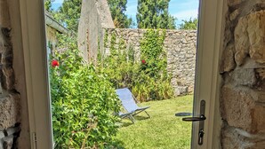 Eine Tür mit Blick auf einen Garten, eine Steinmauer und einen Stuhl.