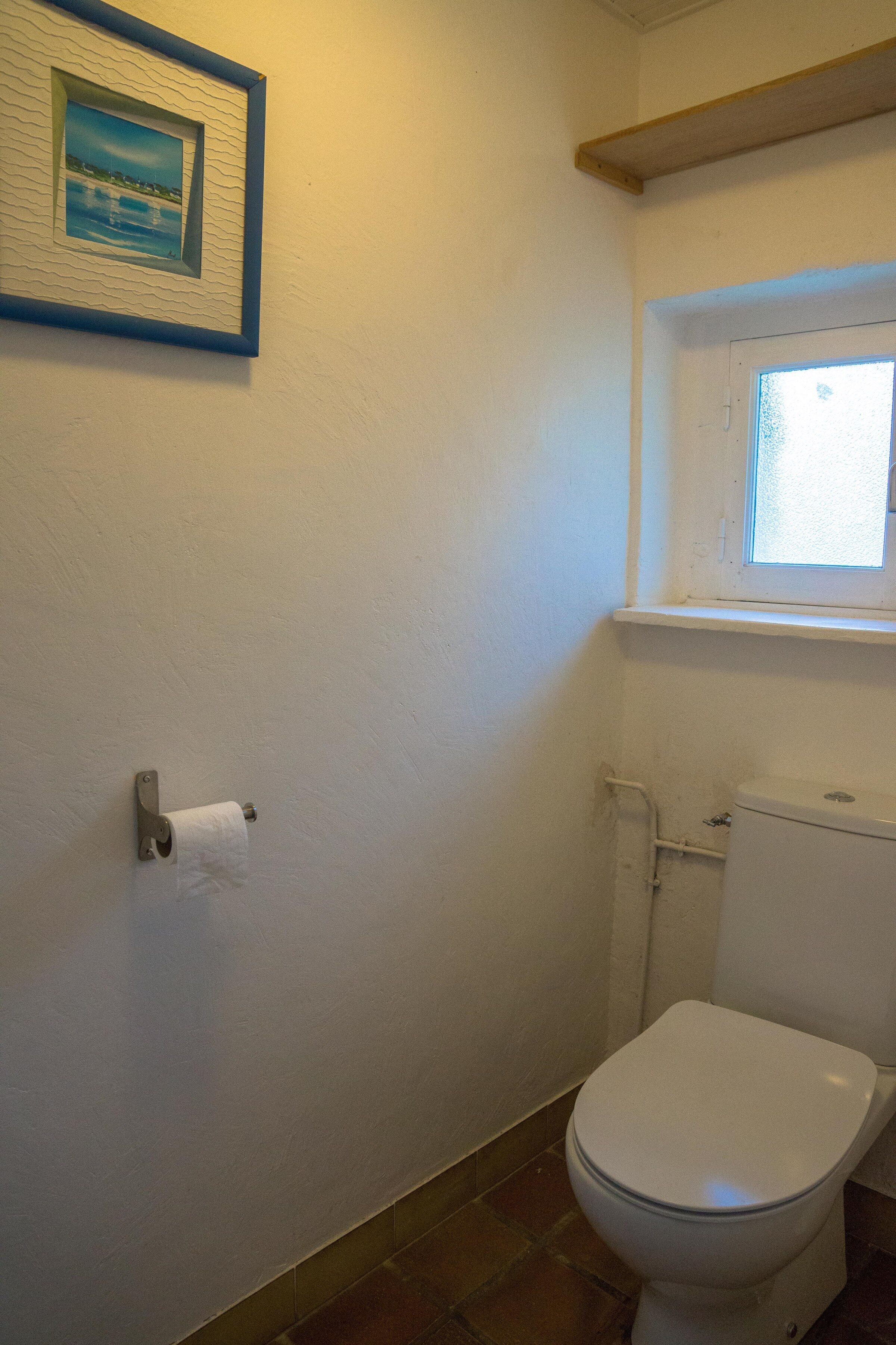 Ein Badezimmer mit Toilette, einem gerahmten Bild an der Wand und einem Fenster über der Toilette.
