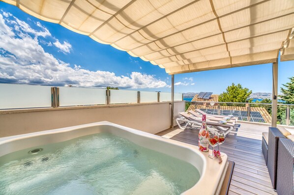 A rooftop terrace with a hot tub, lounge chairs, and a scenic view of the sea and mountains.