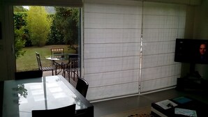 A room with a sliding glass door leading to a garden, a dining table with chairs, and a television on a stand. - HOUSE QUIET, COMFORTABLE, LUMINOUS (Cesson-Sévigné)