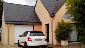 A white car parked in front of a building with a garage door and a potted plant nearby. - HOUSE QUIET, COMFORTABLE, LUMINOUS (Cesson-Sévigné)