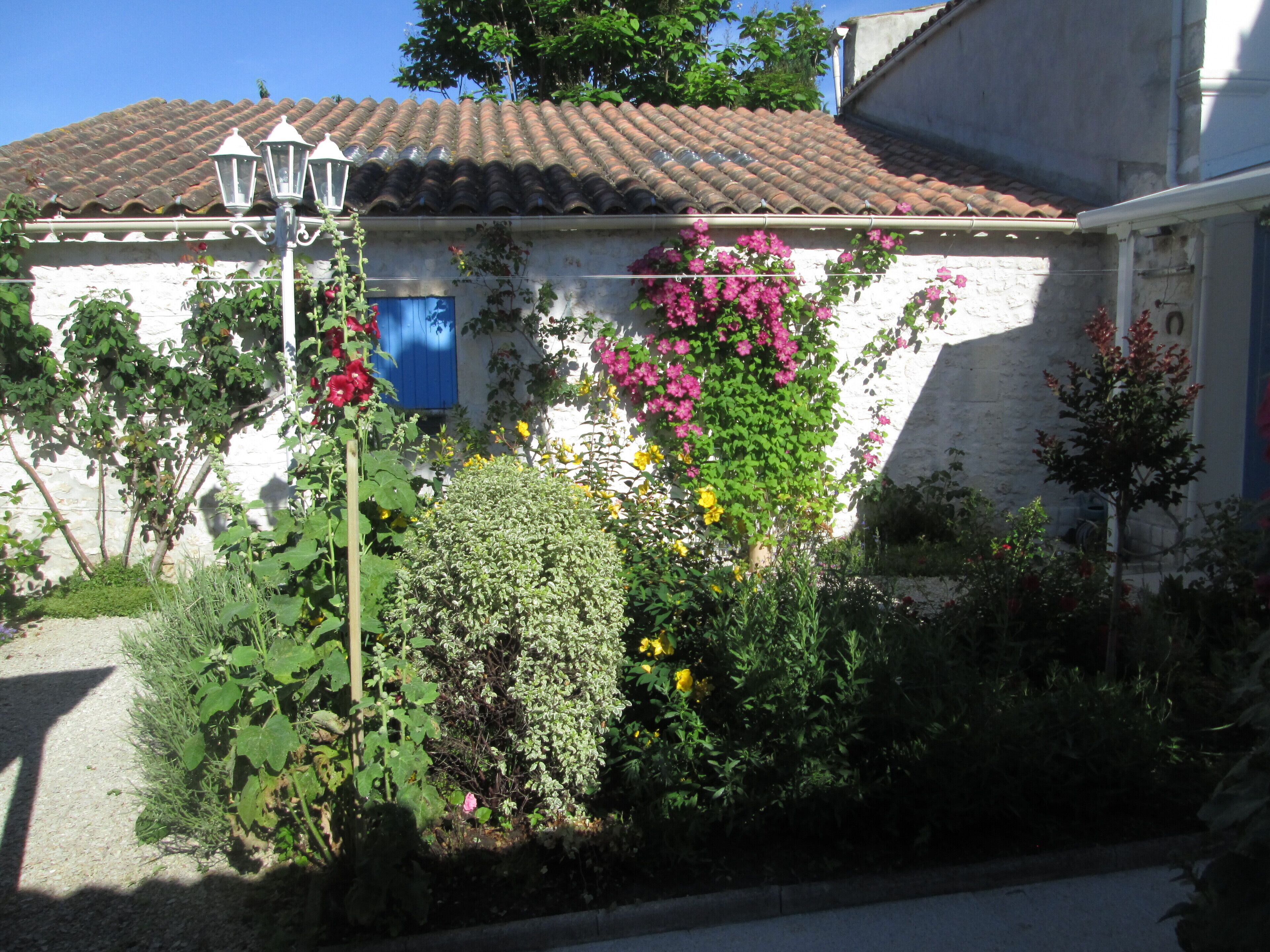 A white house with a tiled roof, a blue door, and a garden with various plants and flowers.