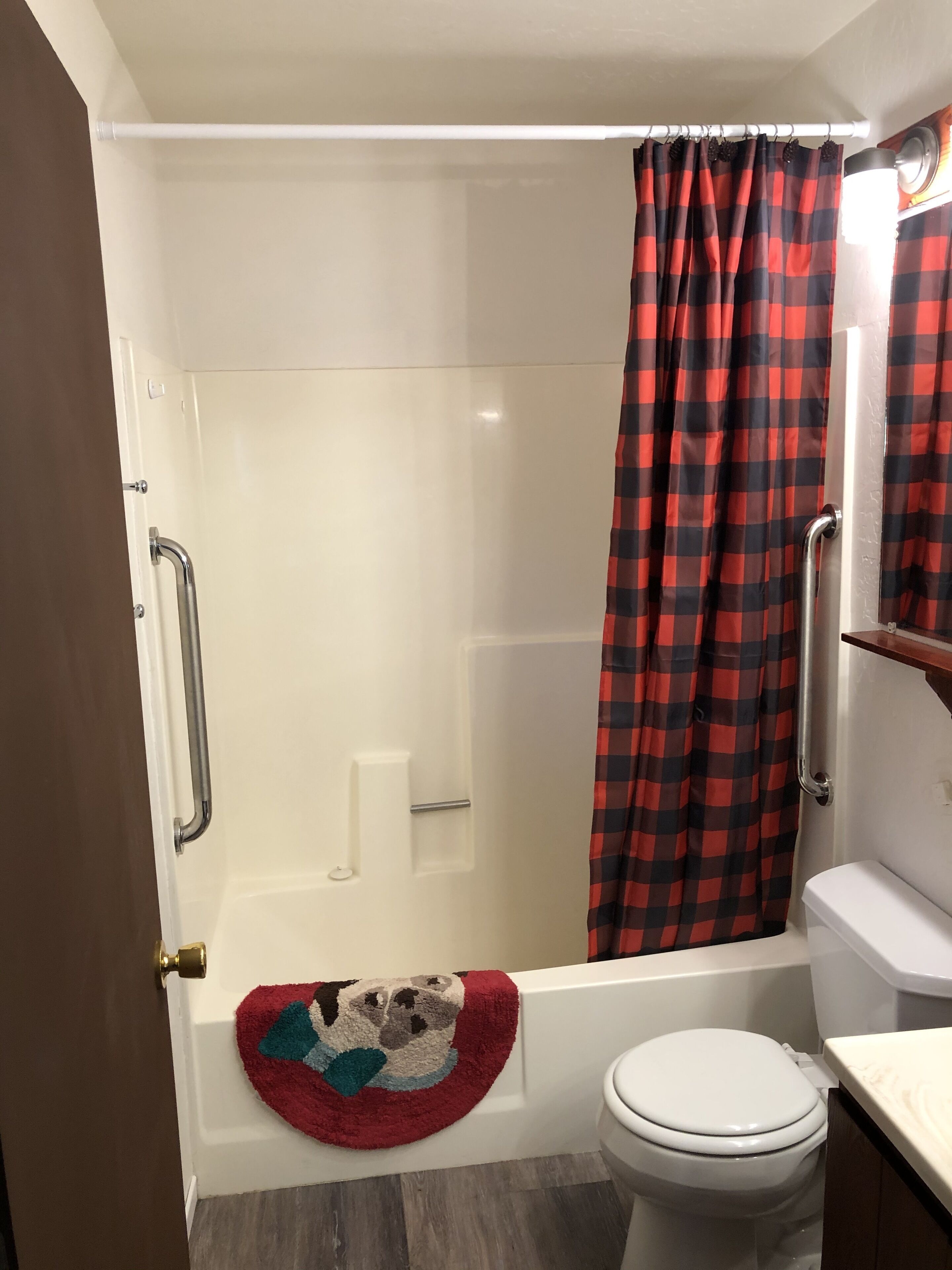 Ett badrum med en dusch som är avskärmad med glasväggar, en vit toalett och ett rött och svartrutigt duschdraperi.