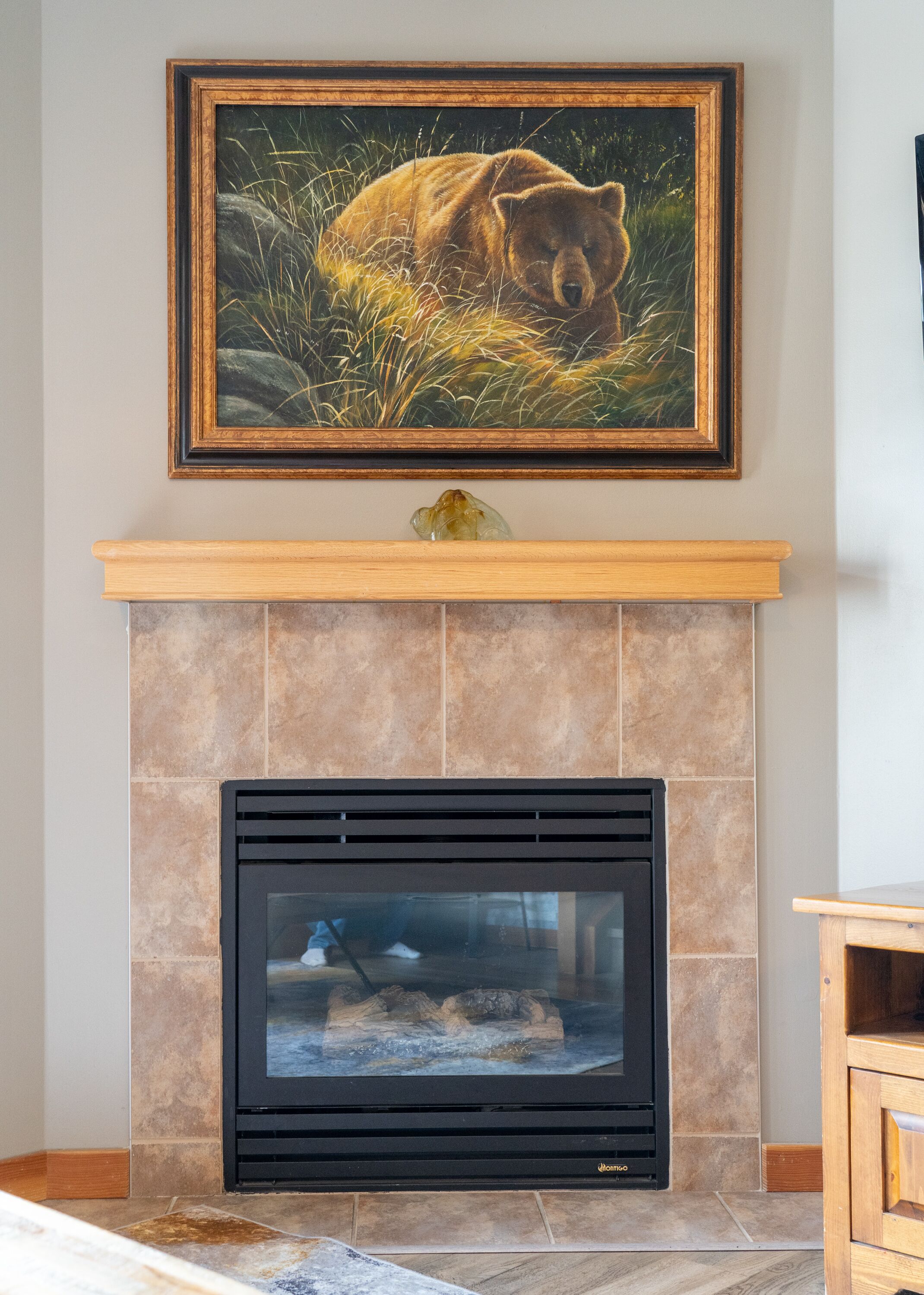 A fireplace with a stone surround, a framed painting above it, and a mantelpiece with a decorative object.