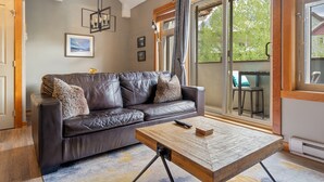 A living room with a leather sofa, a wooden coffee table, and a large sliding glass door leading to an outdoor area. - Canmore Penthouse Loft / Round  Heated Outdoor Pool (Canmore)