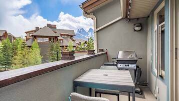 A balcony with a grill, a table, and chairs, overlooking a mountainous landscape.