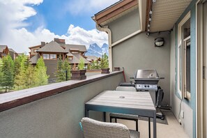 Un balcón con una parrilla, una mesa y sillas, con vista a un paisaje montañoso.