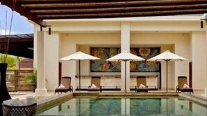Un espace piscine avec des chaises longues et des parasols, un sol carrelé et un mur décoratif.