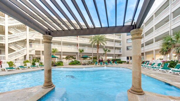 Un espace piscine doté de plusieurs niveaux de balcons, de chaises longues et de palmiers.