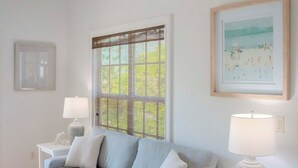 A living room with a grey sofa, two white lamps, a framed picture, and a window with a mesh screen. - Beach Access, heated pool, and new spa. Pickleball and playground along the bay! (Bradenton Beach)