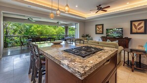 A spacious kitchen with a large island, modern pendant lights, and a view of lush greenery.