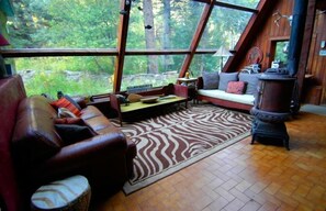Un intérieur de chalet chaleureux avec une grande fenêtre, des meubles en bois et une cheminée centrale.