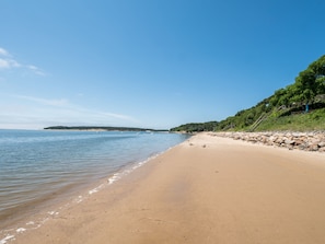 A sandy beach with calm water, a clear sky, and a rocky hillside with trees. - Private Beach. Big Beach house. Kayaks. SUP boards. (wellfleet)
