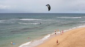 Een strand met mensen en een kitesurfer in het water.
