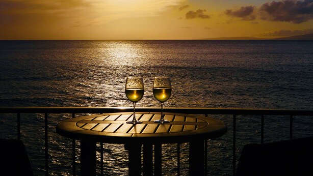 Een tafel met twee wijnglazen, met uitzicht op een zonsondergang boven de oceaan.