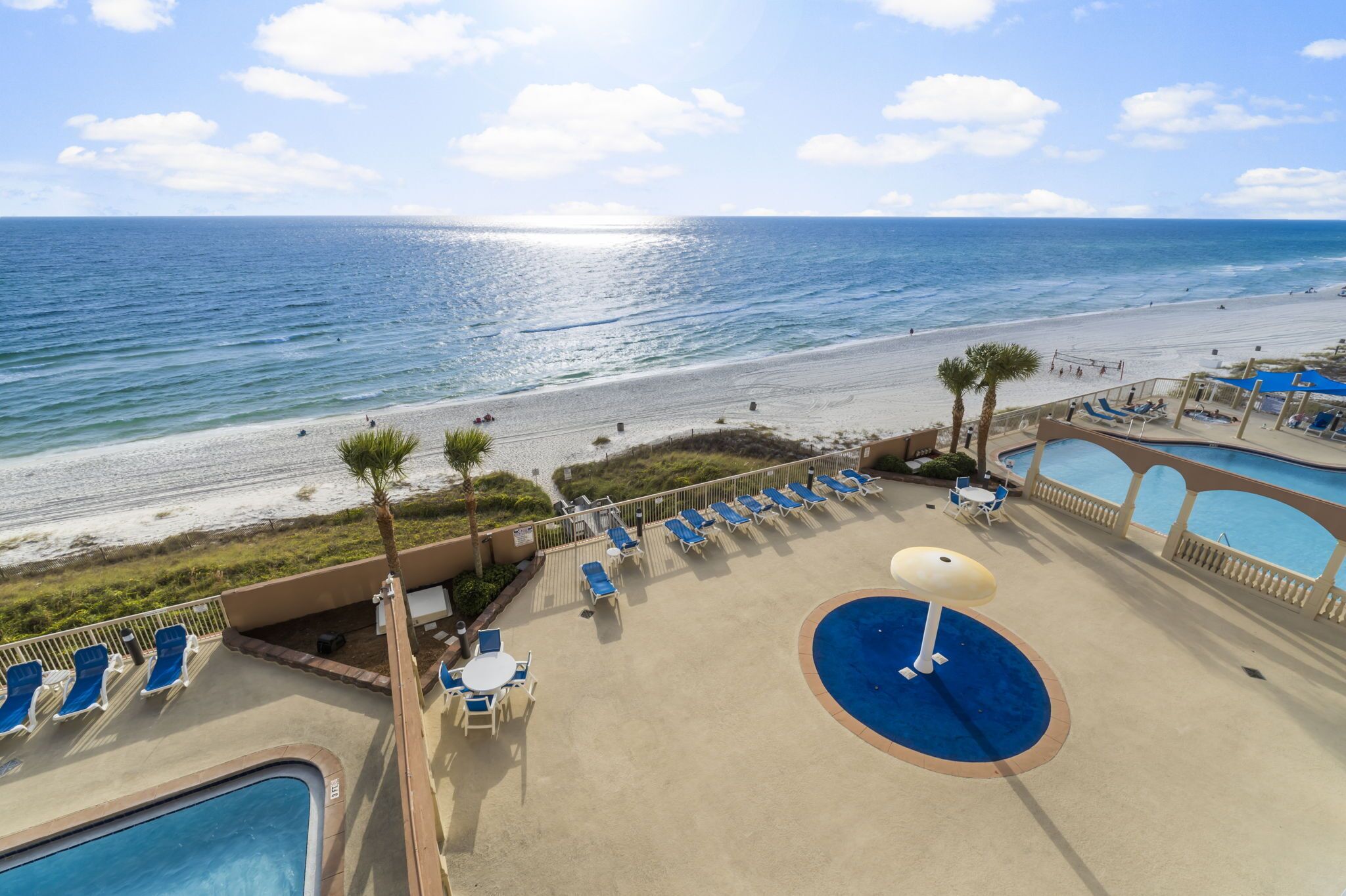 Ein Poolbereich mit Liegestühlen und Sonnenschirmen mit Blick auf einen Strand und das Meer.
