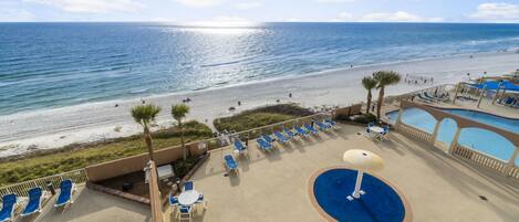 A pool area with lounge chairs and umbrellas, overlooking a beach and ocean.
