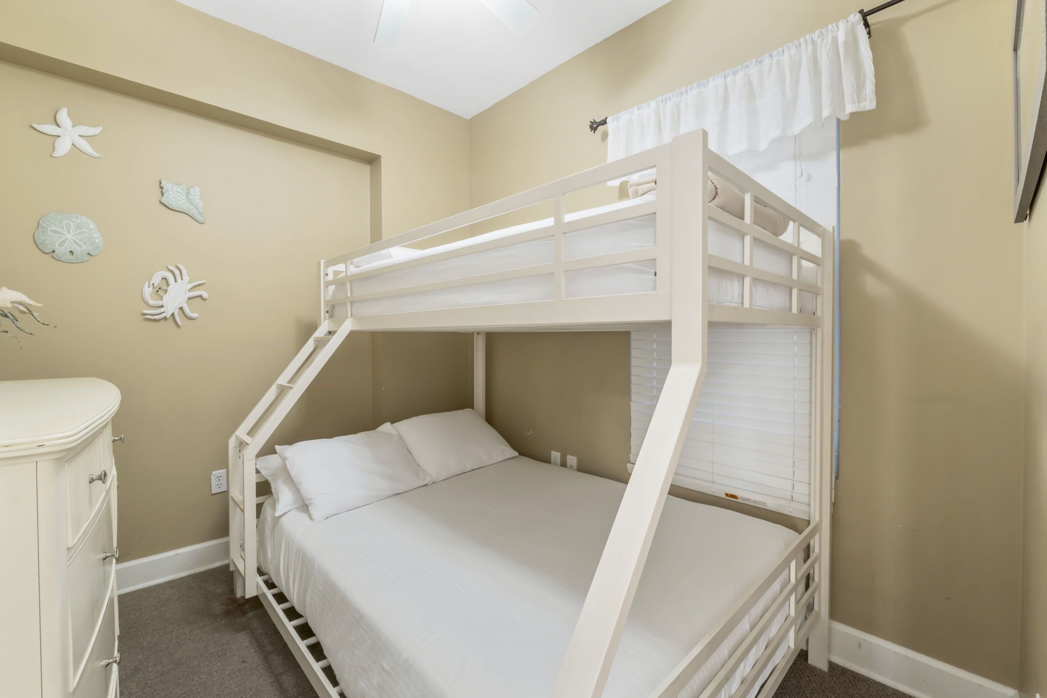 A bunk bed with white bedding, a dresser, and decorative shells on the wall.