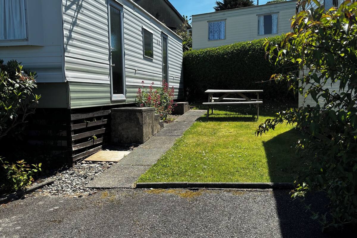A caravan with a satellite dish, a picnic table, and a well-maintained lawn.