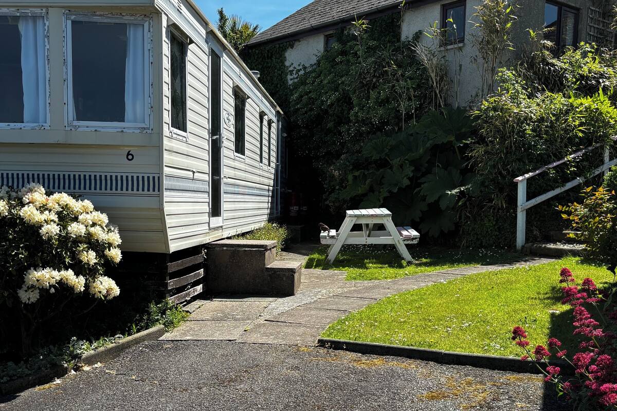 A mobile home with a paved driveway leading to a picnic table and a grassy area.