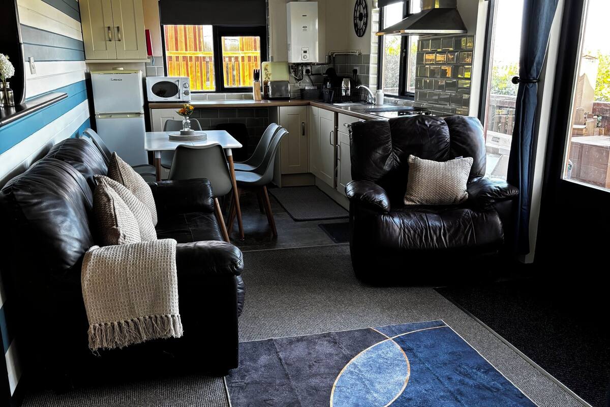 A compact living space with a kitchenette, a sofa, a dining area, and a view through large windows.