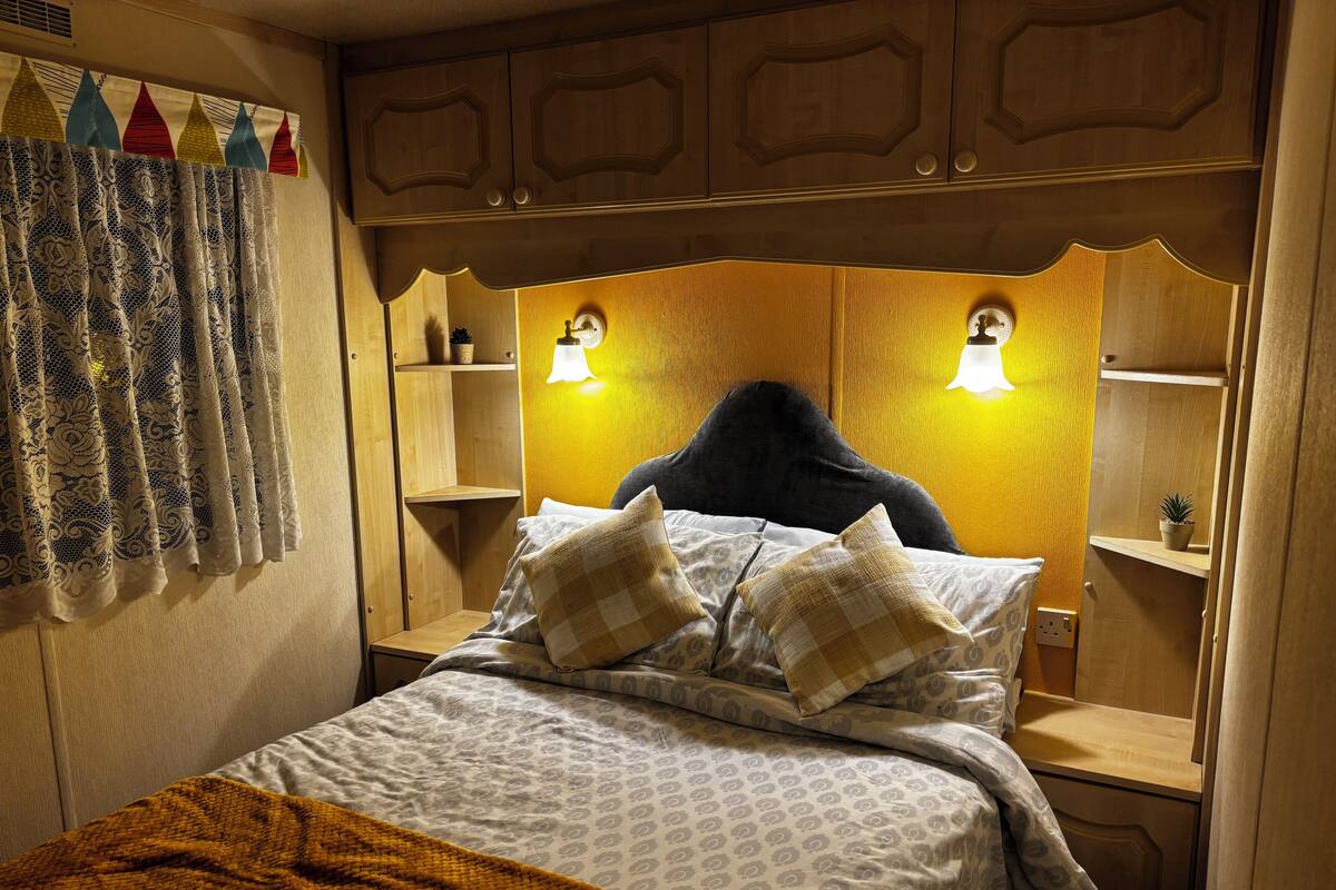 A bedroom with a bed, pillows, a nightstand, a lamp, a window with curtains, and a wooden headboard.