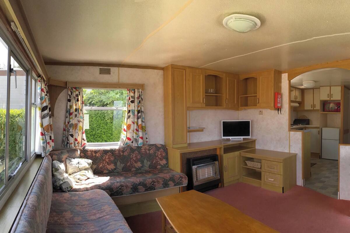 A compact RV interior with a sofa, kitchenette, and a small dining area.