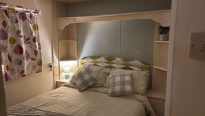 Un dormitorio con cama, lámpara de noche, mesita de noche y ventana con cortina.