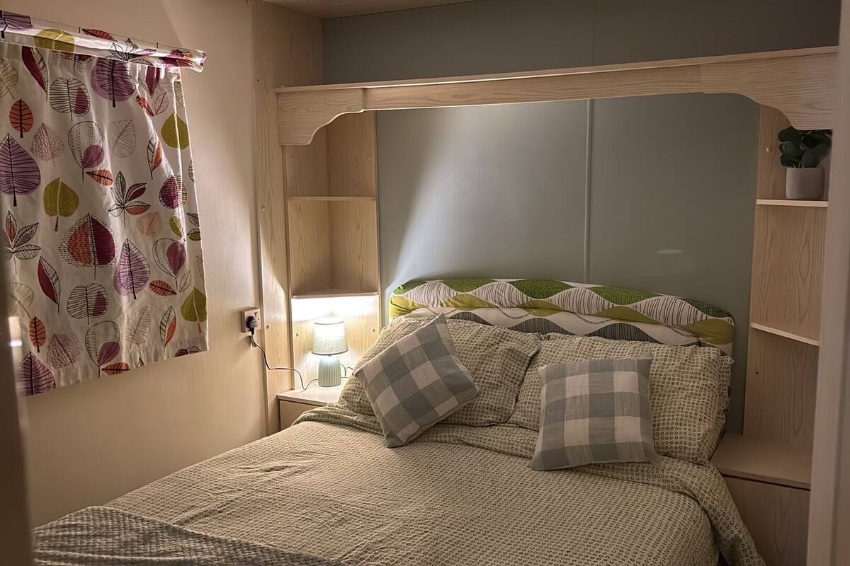 A bedroom with a bed, a bedside lamp, a nightstand, and a window with a curtain.
